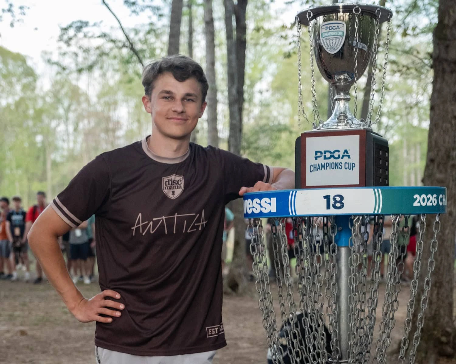 Niklas Anttila leaning on the basket beside the PDGA Champions Cup trophy
